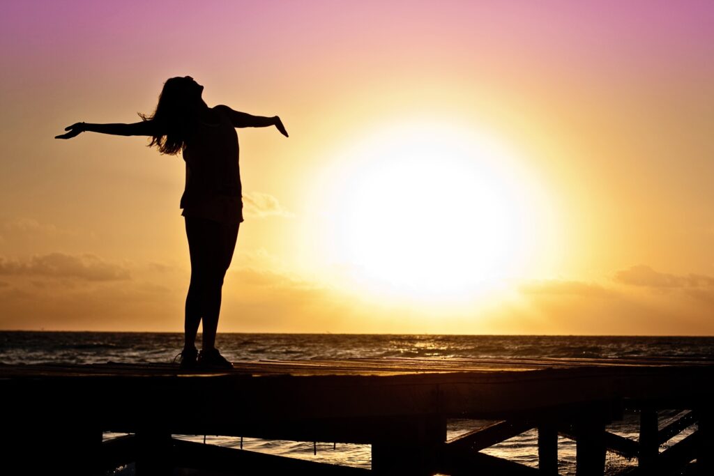 Shadow image of a girl standing on beach with sunset in back ground, she is happy and free with  arms open